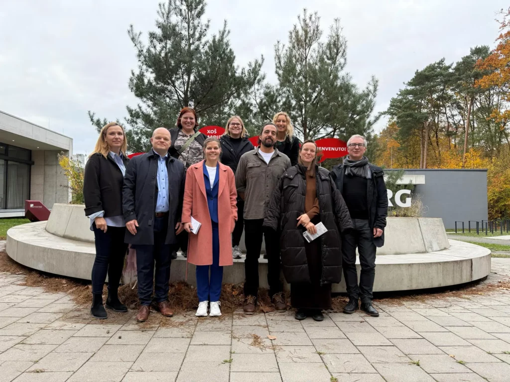 Neun gut gekleidete Männer und Frauen mittleren Alters posieren beim Ausflug auf den Forschungscampus im Hamburger Westen für ein Gruppenfoto und lächeln in die Kamera.