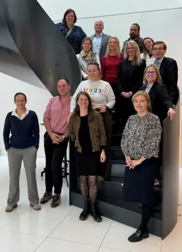 Vierzehn lächelnde Männer und Frauen mittleren Alters posieren auf einer beeindruckenden Wendeltreppe für ein Gruppenfoto.