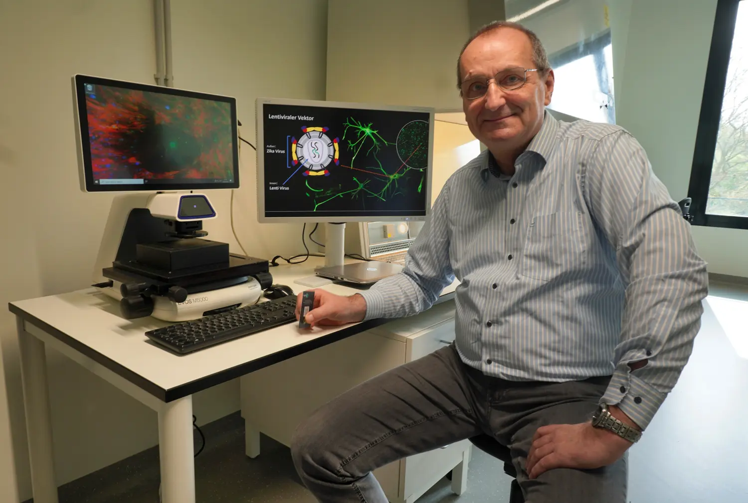 Zilentix-Ceo Dr. Michael Schreiber sitzt an einem Schreibtisch mit Computerbildschirmen und wissenschaftlichen Darstellungen, lächelt in die Kamera.