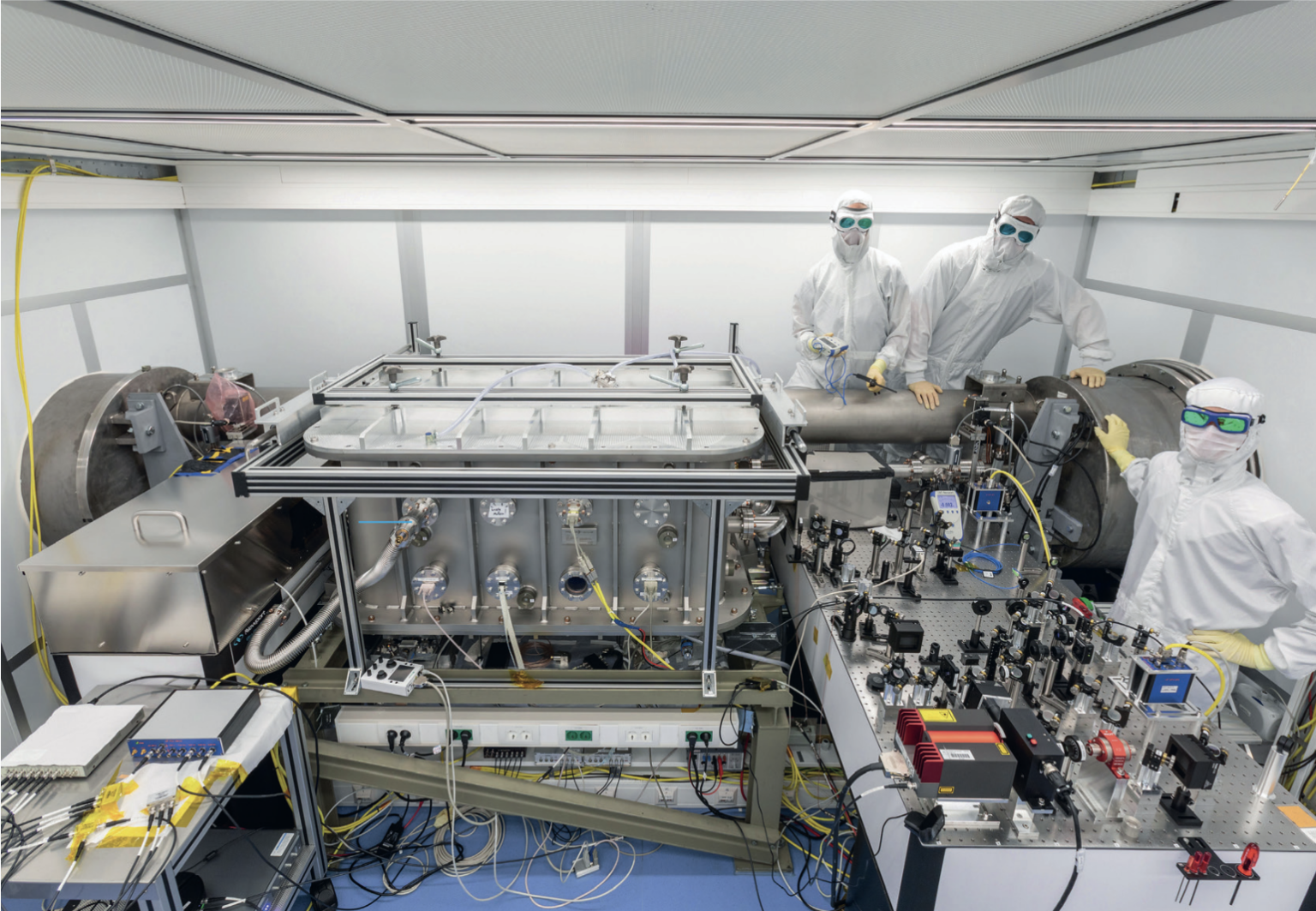 A view inside the cleanroom, showing three female researchers in protective gear and a technical experimental setup.