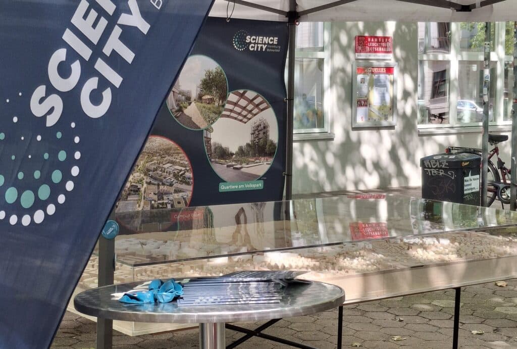 Stand der Science City Hamburg Bahrenfeld auf der altonale mit Fahne, Banner, Tisch und Sitzgelegenheit.